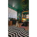 A stylish living room featuring a black and gray wool runner rug with flowing patterns. The contemporary area rug adds a touch of elegance to the space, complemented by a cozy armchair, decorative plants, and a large mirror. Ideal for a vintage or modern living room ambiance.