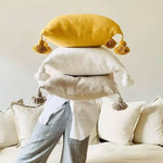 Handmade Boho throw pillows stacked together, featuring pom pom tassels in yellow, white, and beige colors, perfect for adding a cozy touch to any living space.