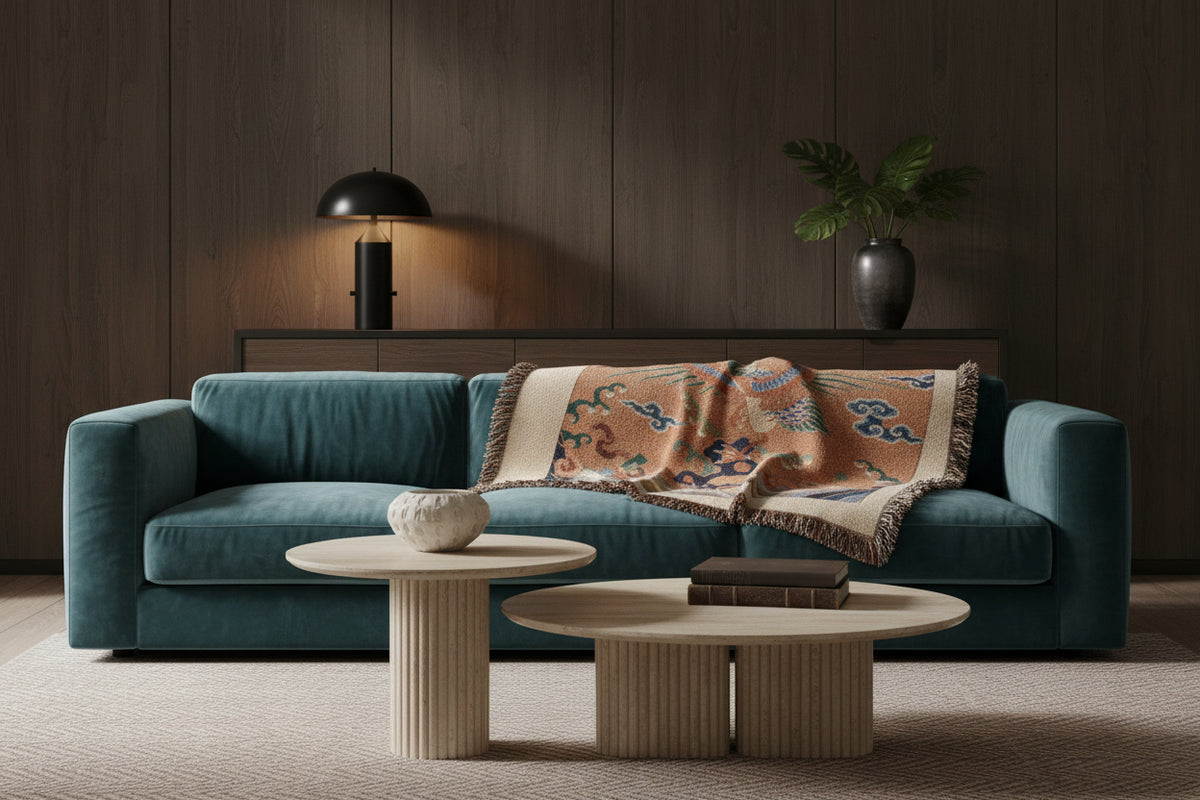 A square woven throw blanket with fringed edges, featuring a central tapestry-style design of a bird among clouds and waves on a warm tan background.