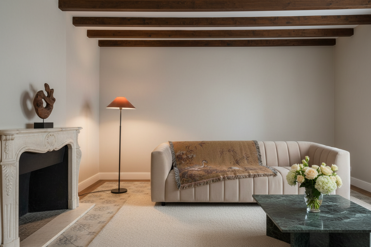 A modern living room featuring a beige tufted sofa with a brown patterned throw blanket, a white fireplace on the left, a black marble coffee table with a flower arrangement, and a floor lamp with a conical shade.