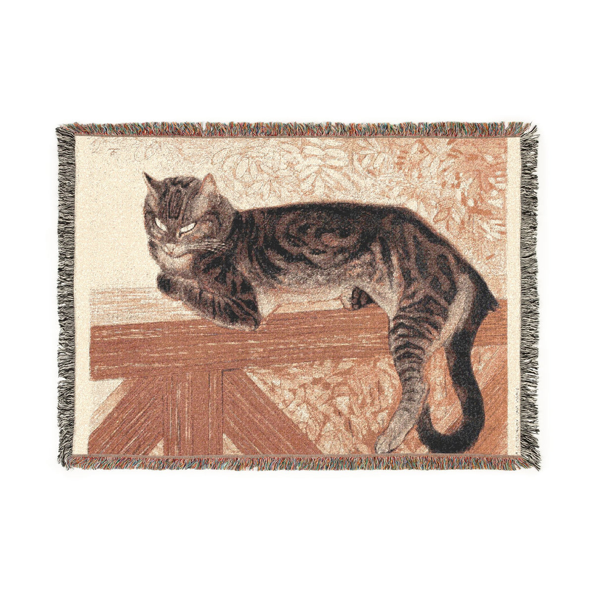 A rectangular woven throw blanket with fringe edges, featuring a detailed illustration of a brown tabby cat lying on a wooden surface against a warm beige and rust background.