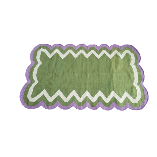 This is a handmade cotton area rug featuring scalloped edges in vibrant shades of purple and green. The rug is crafted with meticulous attention to detail, showcasing intricate scalloped patterns that add a touch of elegance to any room. Made from soft and durable cotton material, this rug is both functional and stylish, offering comfort and a pop of color to your living space.