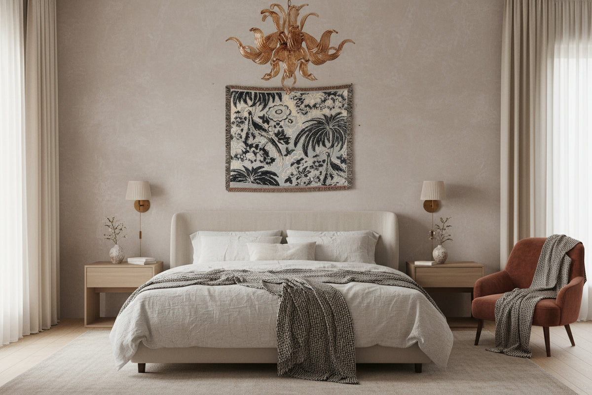 A square woven throw blanket featuring a classic French Toile pattern with palm trees, peacocks, and floral motifs in black and gray on a light beige background, finished with fringed edges.