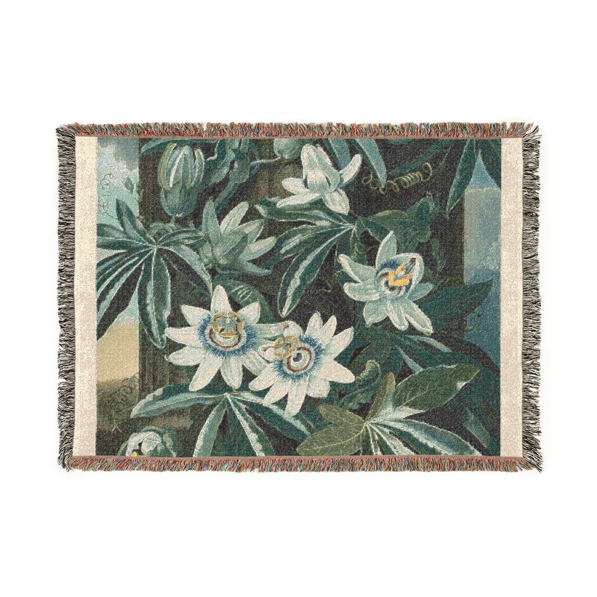 A woven tapestry throw blanket featuring a botanical design of white passion flowers and green leaves on a dark background, finished with fringed edges.