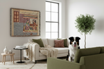 A framed tapestry with Arabic calligraphy and a traditional scene hangs on a white wall in a modern living room. A black and white dog sits on the floor in the foreground, looking toward the tapestry.