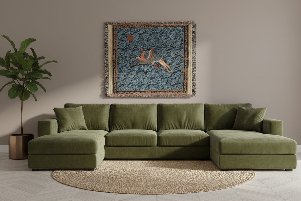 A square woven throw blanket with fringe, featuring a detailed tapestry-style design of a flying crane or heron over wavy clouds under a red sun, set against a blue background.