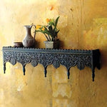 Carved dark wood wall shelf with ornate fretwork apron on mustard wall