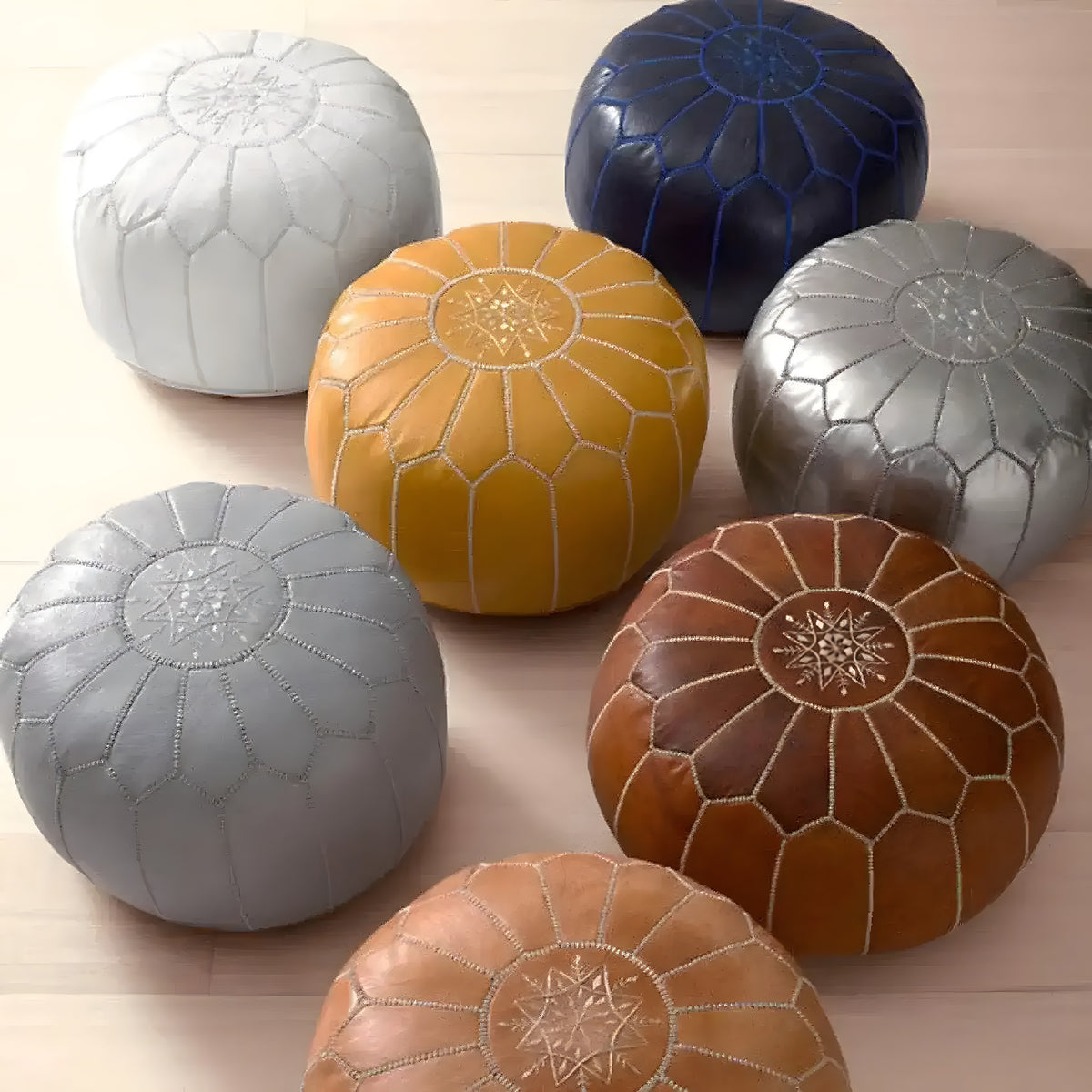 Seven round Moroccan leather pouf covers in silver, navy, mustard, gray and tan on a floor