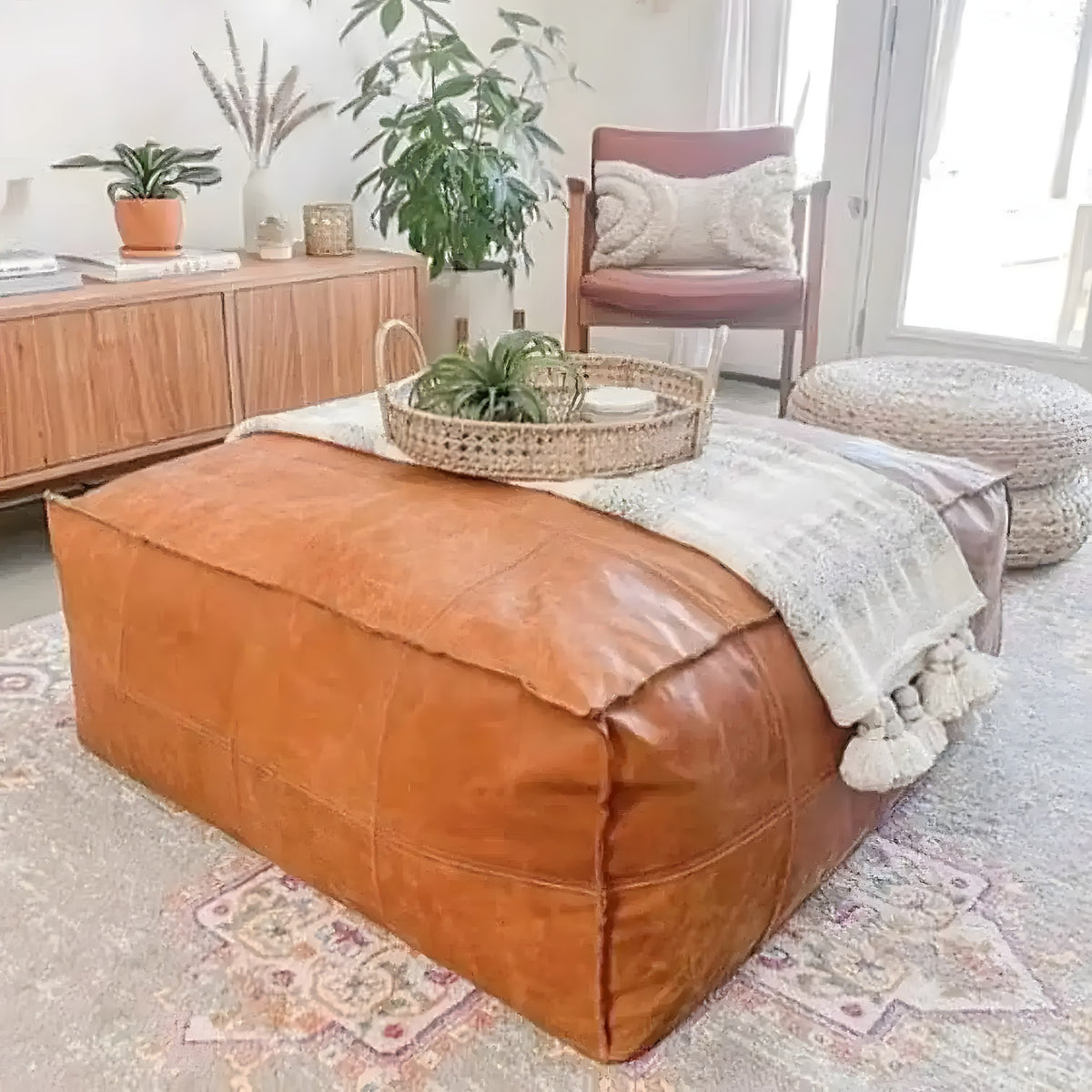 Square tan leather Moroccan pouf as a coffee table with a rattan tray and plant on a rug