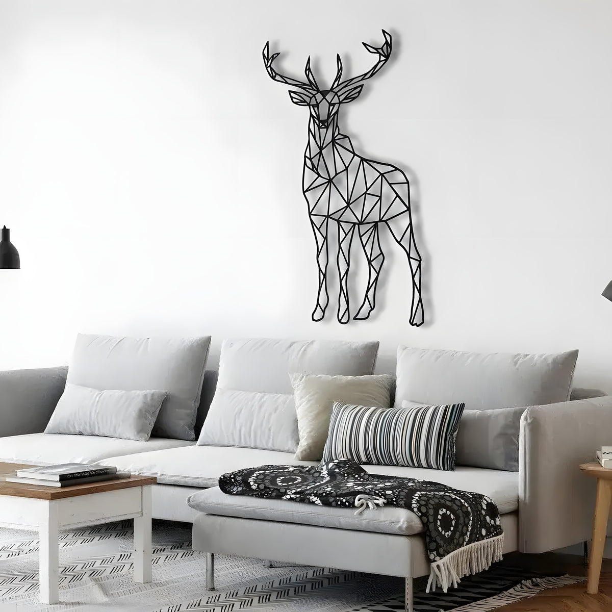 Black geometric deer metal art with polygon antlers on a white wall above a gray sofa