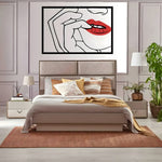 Black line-art metal wall art of a hand at parted red lips, framed, above a bed