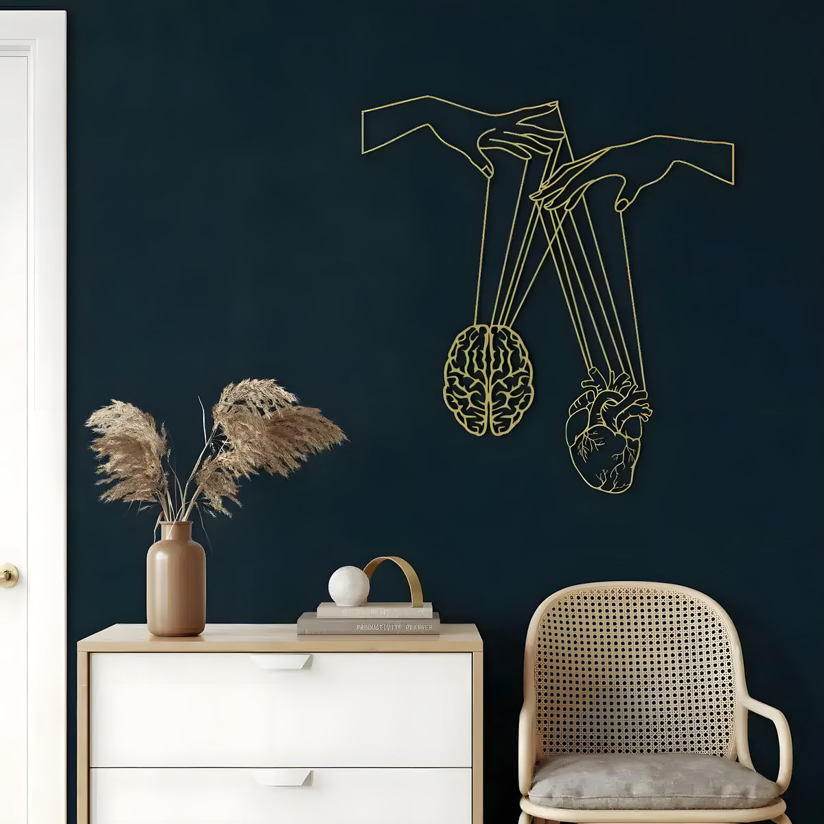 Gold brain and heart metal wall art of hands holding strings on a navy wall above a dresser
