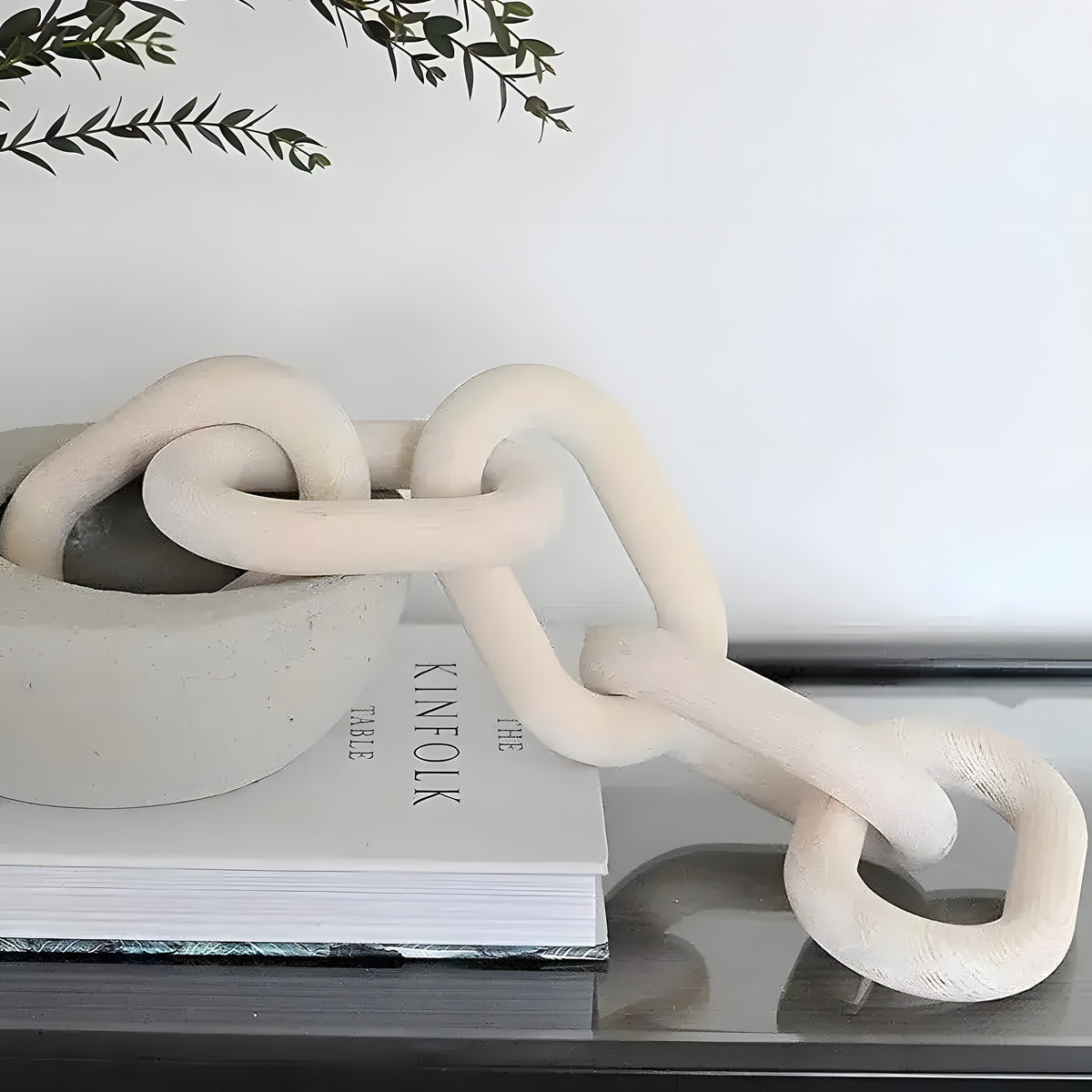 Whitewashed carved wood chain link decor draped over a concrete bowl and book on a glass table
