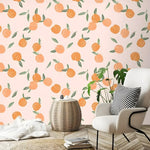 Peach fruit wallpaper on blush pink behind a white accent chair and rattan side table