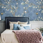 Blue chinoiserie floral and bird wallpaper behind a navy headboard with pink knit throw
