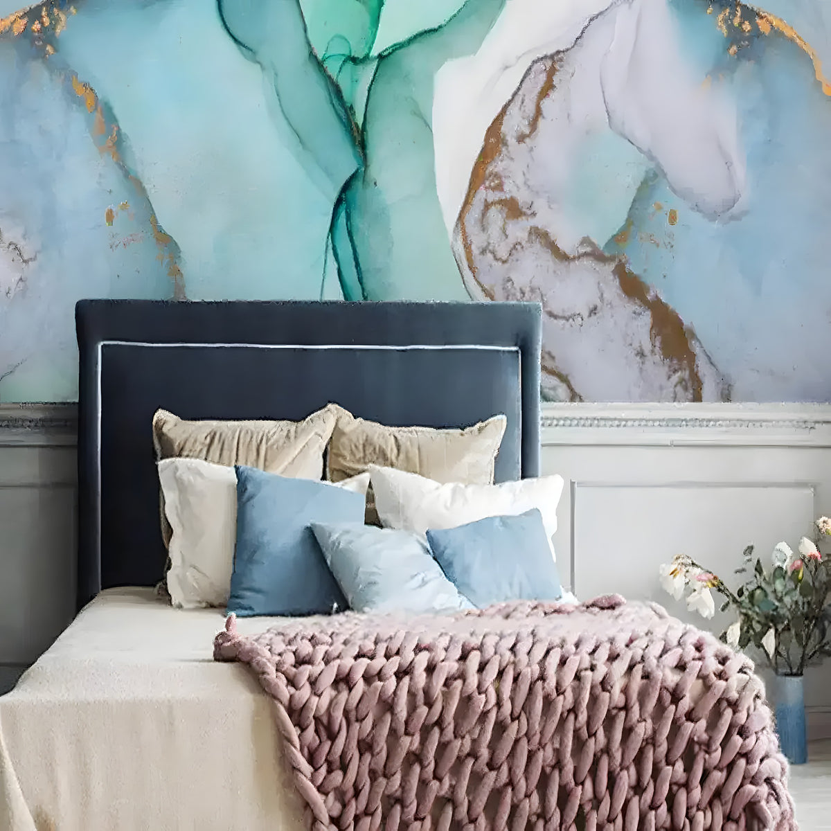 Teal and mint marble ink mural with gold veining above a navy upholstered headboard with cream and blush knit throw