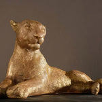 Gold reclining leopard sculpture, head raised and front paws crossed, on dark backdrop
