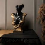 Black and gold female bust sculpture, head tilted back with gold drape across the chest