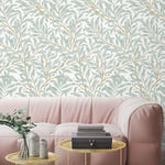 Willow leaves wallpaper in soft sage green and gold behind a blush pink sofa