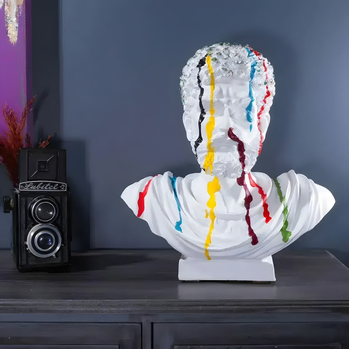 White Marcus Aurelius bust with silver hair and rainbow paint drips on dark sideboard