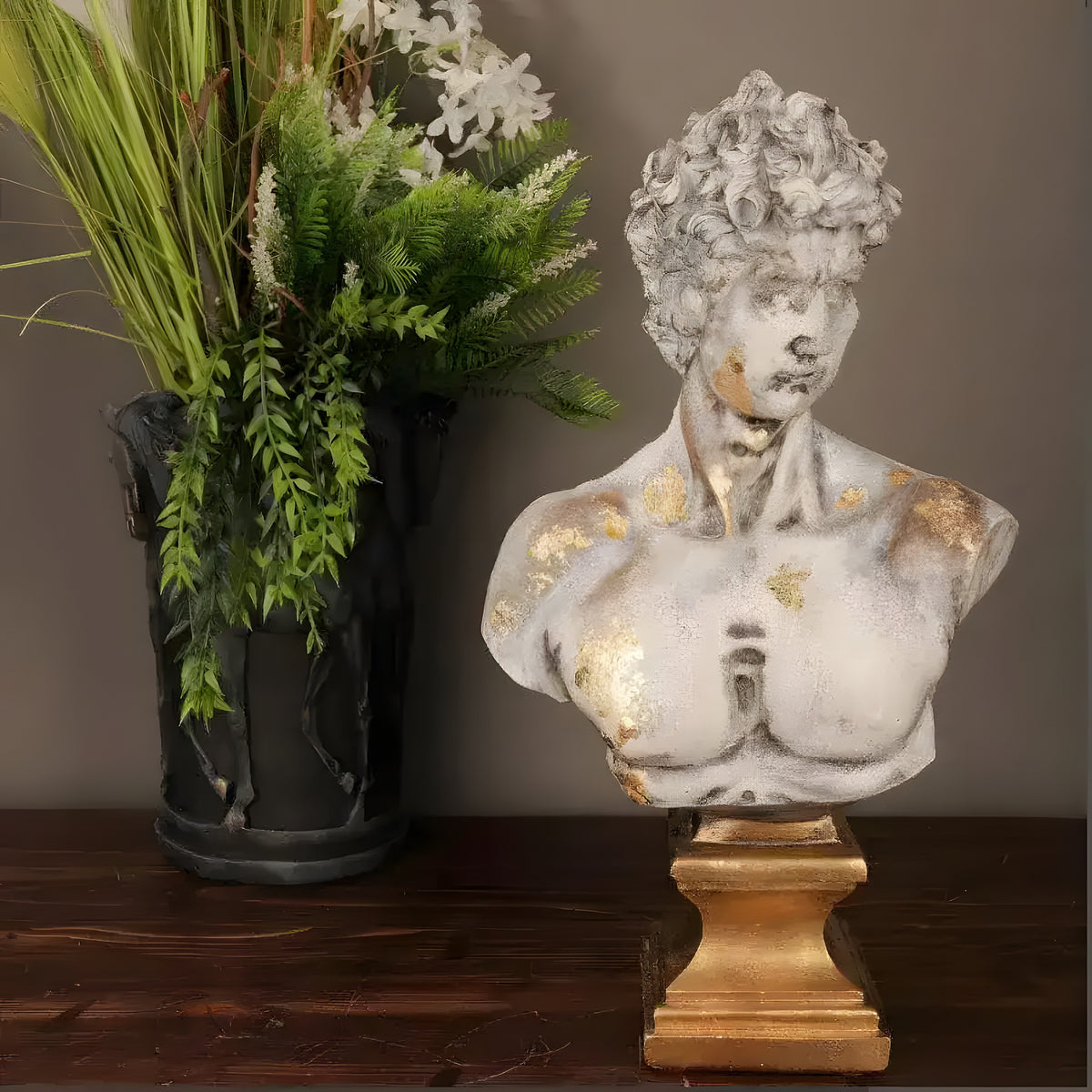 Distressed white David bust with gold-leaf flecks on gold pedestal by greenery