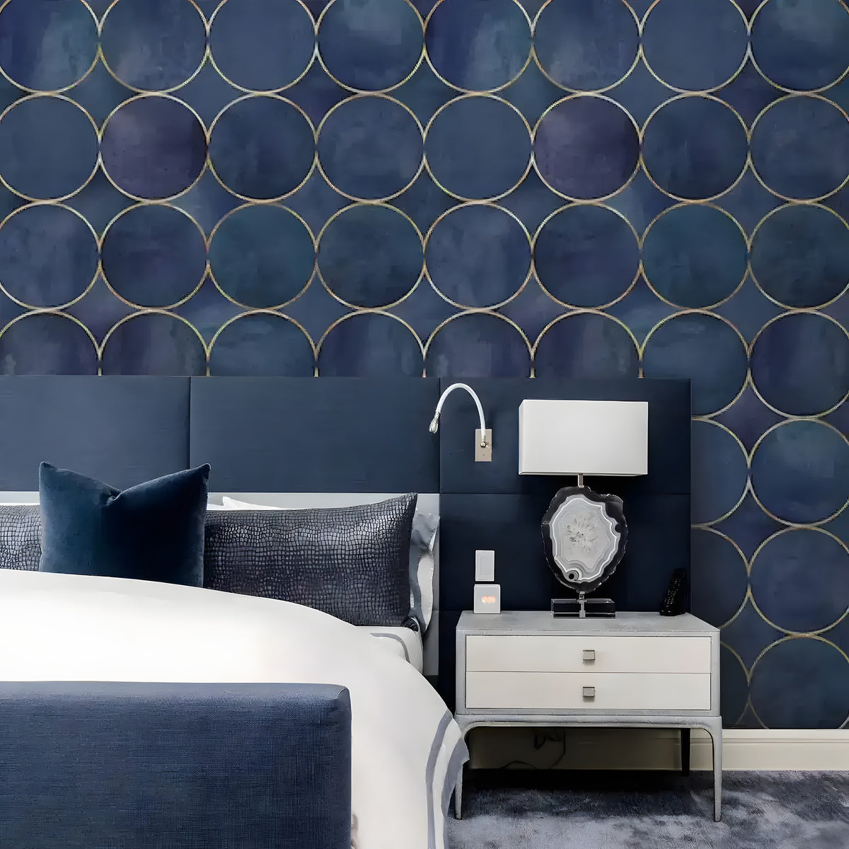 Navy watercolor circles mural with gold outlines behind upholstered bed and agate lamp