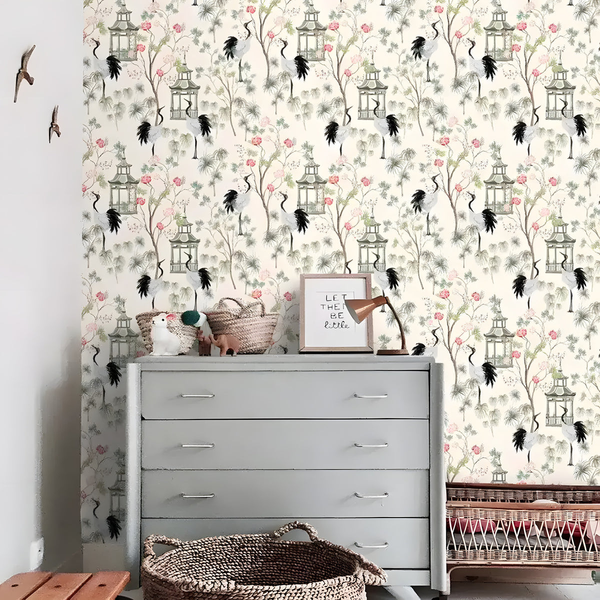 Chinoiserie cranes and pagodas wallpaper behind gray dresser in nursery