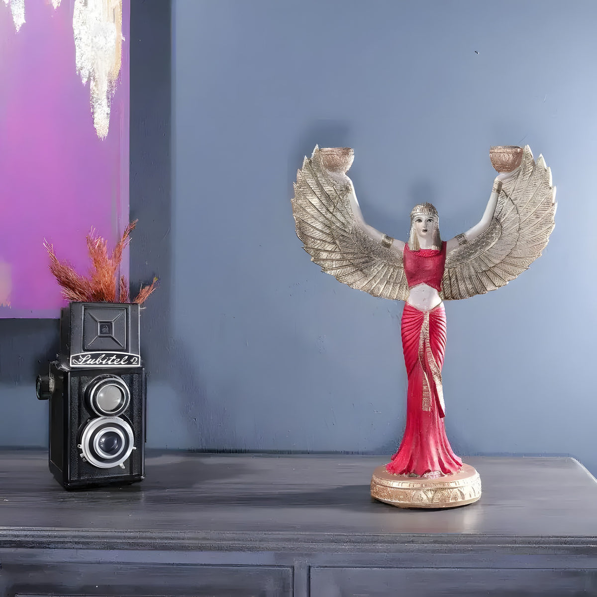 Standing Isis goddess sculpture in red dress with gold feathered wings holding two candle bowls, on a console