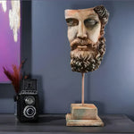 Weathered stone Zeus bust sculpture with bearded face on a rod and square base, on a dark console