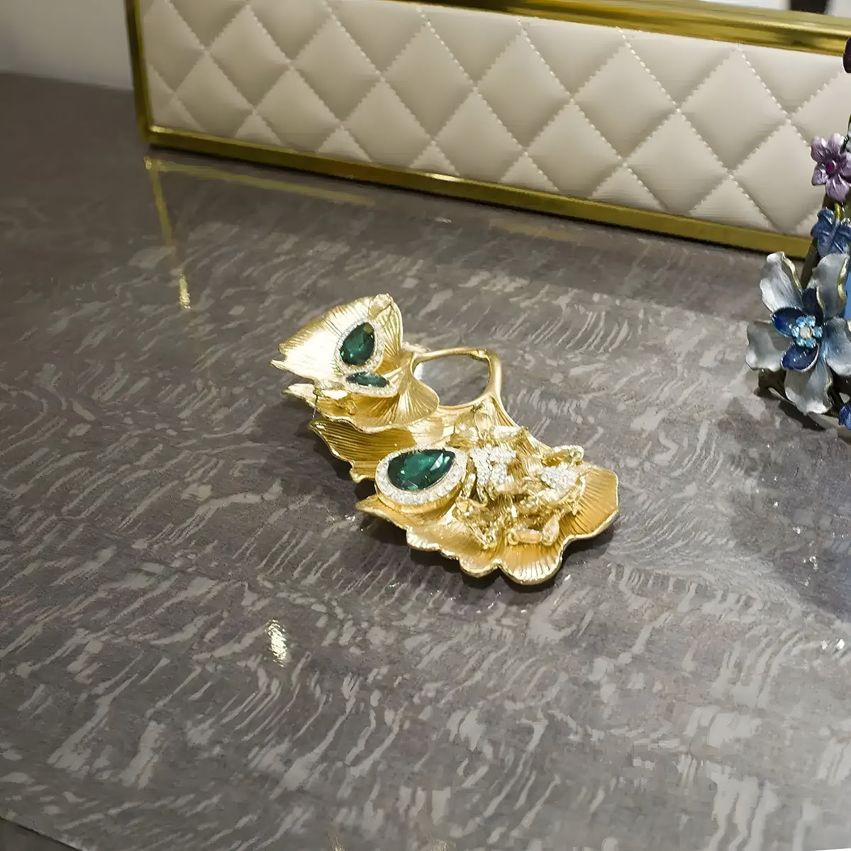 Gold gingko-leaf trinket dish with emerald and clear crystal accents on grey marble