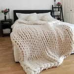 Cream chunky knit merino wool throw blanket draped over a bed with matching knit pillows