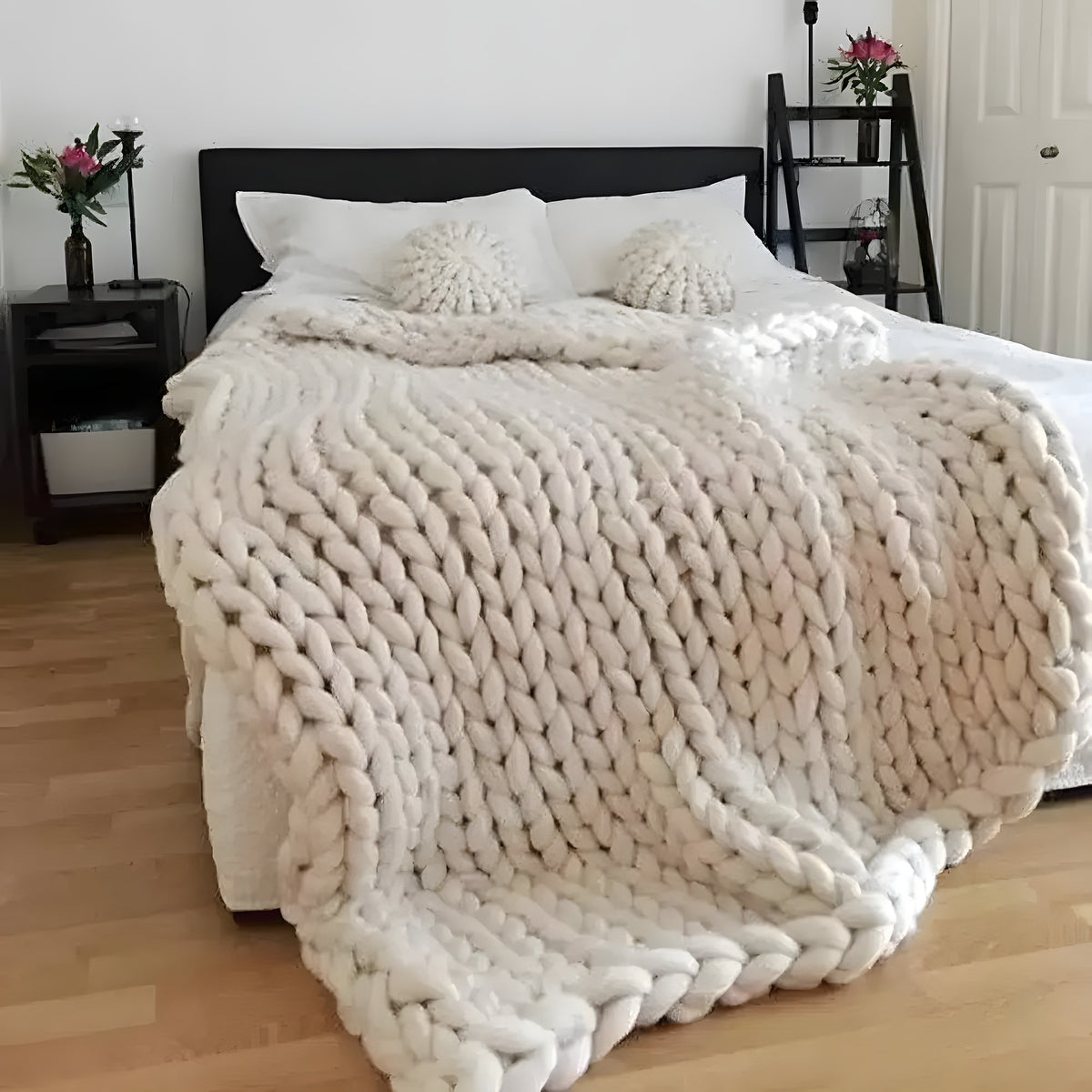 Cream chunky knit merino wool throw blanket draped over a bed with matching knit pillows