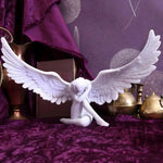 White sobbing angel statue with spread feathered wings, head bowed, on purple velvet