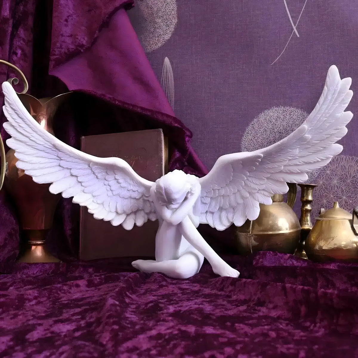 White sobbing angel statue with spread feathered wings, head bowed, on purple velvet
