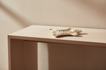 A small decorative ceramic dish with a white and gold zebra-like striped pattern, resting on a light wood console table against a textured beige wall.