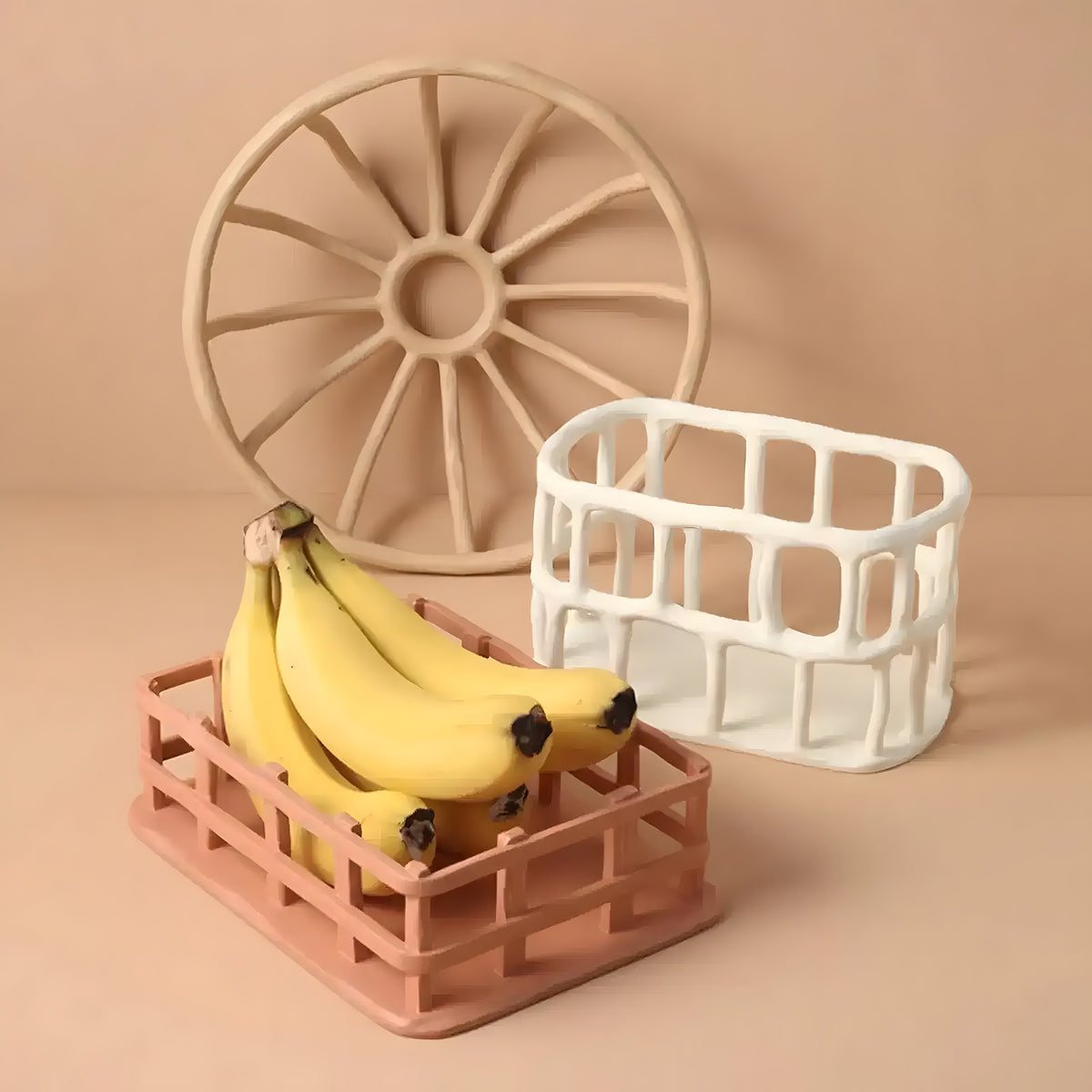 Pink and white hollow resin fruit baskets with bananas and a round trivet, beige backdrop