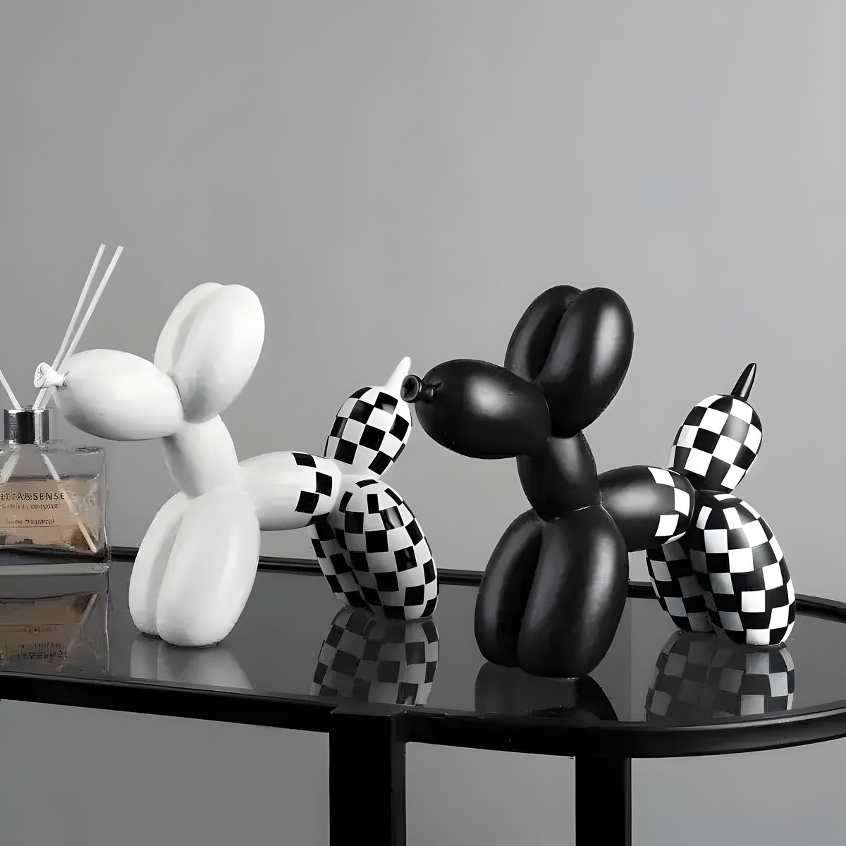 White, black and checkered balloon dog figurines grouped on a black glass table