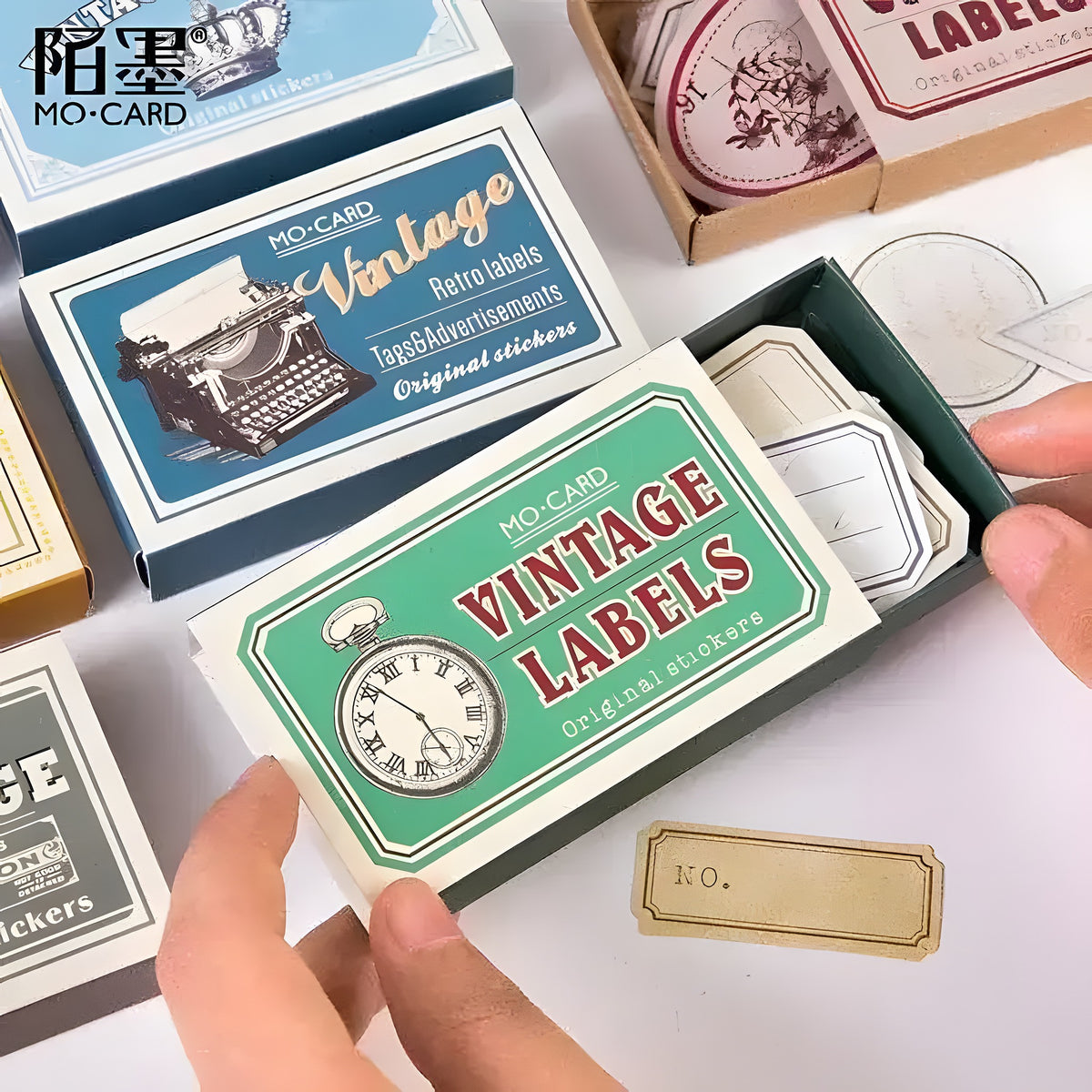 Hands holding matchbox-style Vintage DIY diary stickers boxes with pocket watch and typewriter labels