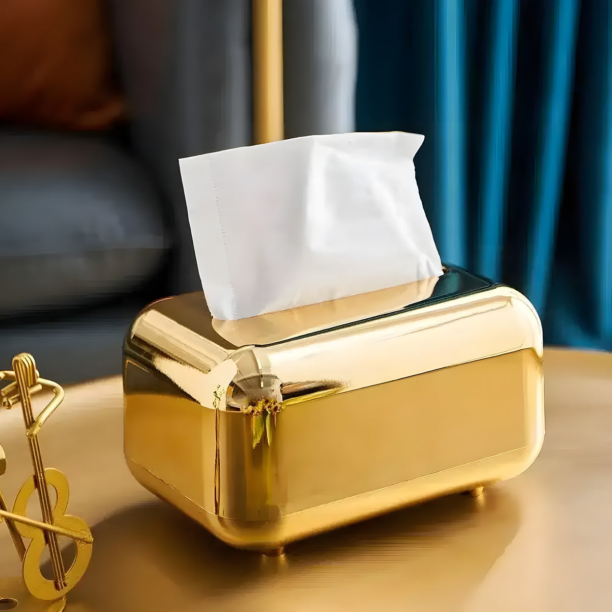 Glossy gold retro tissue box with white tissue, on a side table by a blue velvet curtain