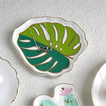 Monstera-leaf ceramic trinket dish in two-tone green with gold trim holding a necklace