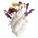 White ceramic anatomical heart vase with colorful dried flowers — purple, yellow, red — emerging from openings