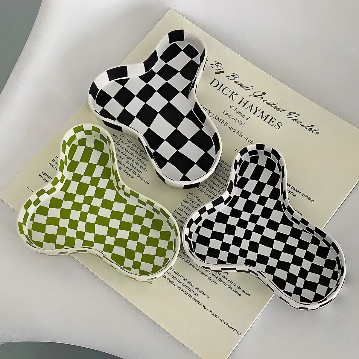 Three chic checkers ceramic bowls — black-white and green-white checker, organic blob shape, stacked on vintage record sleeve
