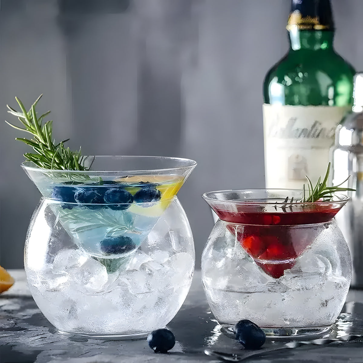 Two interlayer triangle cocktail glasses with ice and garnish — large with blueberries, small with cranberries