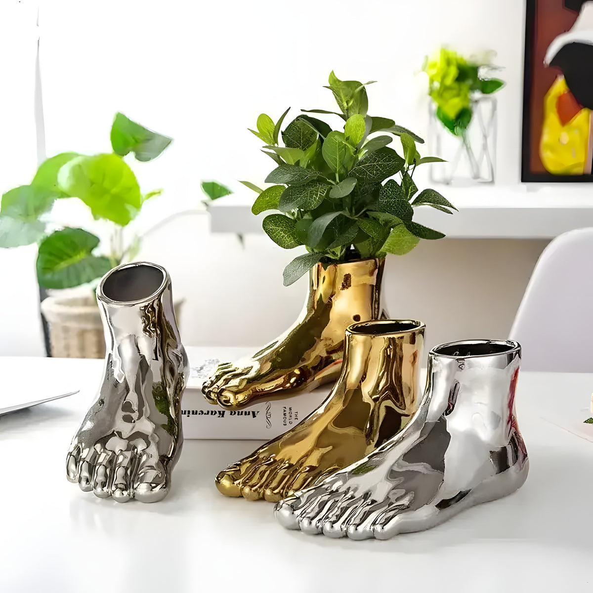 Two silver and one gold foot-shaped planter on white table, gold one holds green plant, indoor decor setting