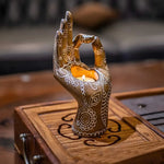 Hand carved buddha mudra candle holder with lit tealight in palm, bronze finish with white henna floral patterns