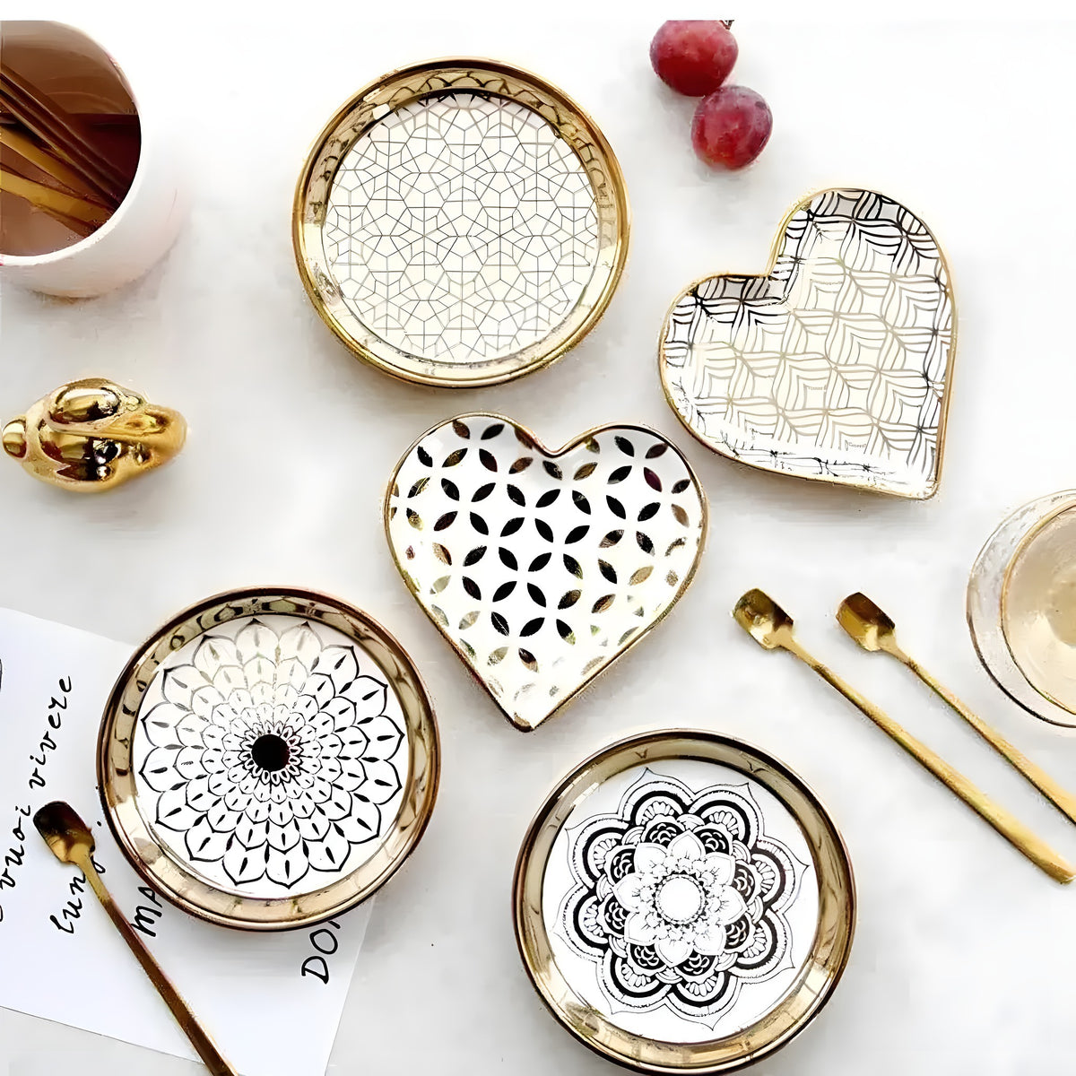Flat lay of four gold plated ceramic dishes — round and heart-shaped with mandala patterns and gold rim borders