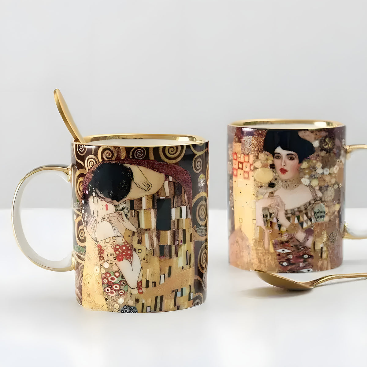 Two Klimt Kiss porcelain mugs with gold-trim handles — The Kiss and Adele portrait paintings — with gold spoons