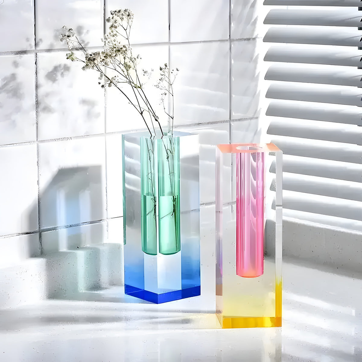 Two rainbow pillar glass bud vases in green-to-blue and pink-to-yellow gradient, holding dried flowers on a white countertop