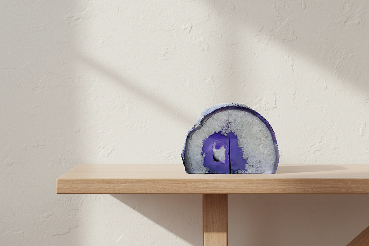 A polished agate stone decorative object with a purple and white geode pattern, displayed on a light wood shelf against a textured beige wall.