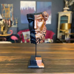 Zeus bust sculpture with black and rose gold two-tone split face on black stand, displayed on wood table
